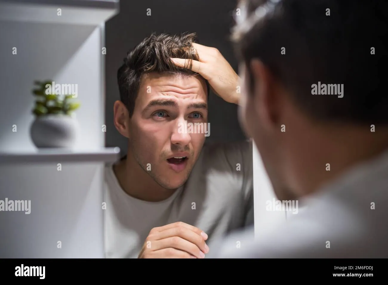 worried-man-is-looking-his-hair-in-the-mirror-2m6fddj Sự lo lắng của nam giới khi nhận thấy dấu hiệu rụng tóc sớm ở tuổi 20